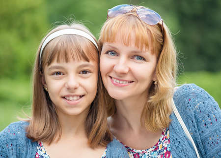 Happy family outdoors in summer day. Mother Day. Portrait of mother and daughter smiling into the camera lens. Woman with child having fun together during walk in the park.の写真素材