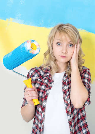 Tired woman at work in the home - painting wall at room. Portrait of woman painting big Ukrainian flag on wall at home.の写真素材