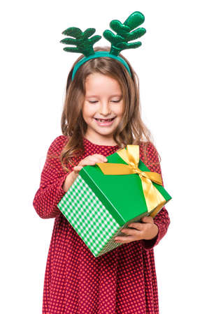 Portrait of laughing little girl with funny Christmas antlers of a deer. Holiday concept - happy cute child holding gift box, isolated on white background.の写真素材