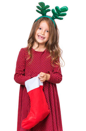 Portrait of caucasian girl with funny Christmas antlers of a deer. Happy schoolgirl, isolated on white background. Holiday concept - funny cute child holding Christmas sock.の写真素材
