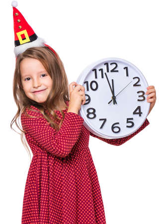 Portrait of a beautiful caucasian little girl wearing small Santa Claus hat, isolated on white background. Holiday Christmas concept - funny child holding big clock.の写真素材