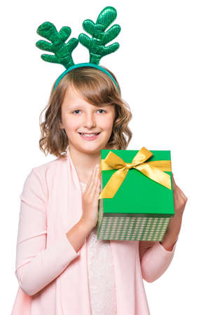 Portrait of laughing little girl with funny Christmas antlers of a deer. Holiday concept - happy cute child holding gift box, isolated on white background.の写真素材
