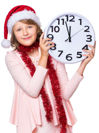 Portrait of smiling little girl with Santa Claus hat. Holiday Christmas concept - happy cute child holding big clock, isolated on white background.の写真素材