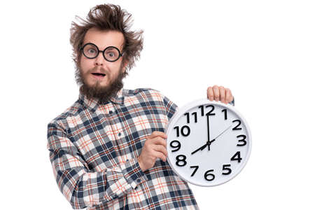 Crazy bearded Man in plaid shirt with funny Haircut in eye Glasses holding Big Clock, isolated on white background. Time concept.の写真素材