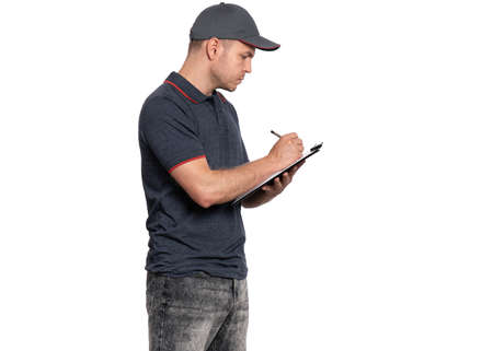 Portrait of Delivery man in cap holding clipboard with papers document and pen, writes. Handsome man Courier isolated on white background.の写真素材