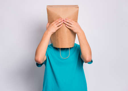 Portrait of teen boy with paper bag over head with hands on face covering eyes. Teenager cover head with bag close eyes with palms posing in studio. Child pulling bag over head. See no evil concept.の写真素材