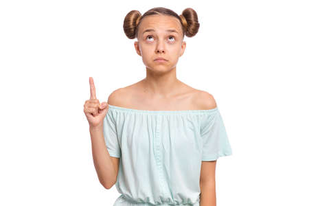 Portrait of teen girl pointing finger up at copyspace, isolated on white background. Beautiful caucasian young teenager attracted by attention pointing finger at something. Surprised or amazed child.の写真素材