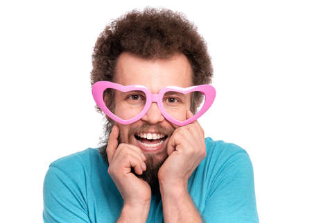 Happy Valentines Day. Crazy bearded Man with funny Curly Hair in heart shaped eye Glasses. Happy and silly guy in Love, isolated on white background. Portrait of Cheerful man looking at camera.の写真素材
