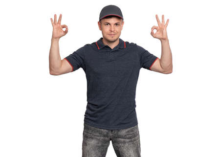 Happy Delivery man in gray t-shirt and cap. Studio portrait of caucasian handsome guy making Ok gesture and looking at camera. Courier isolated on white background.の写真素材