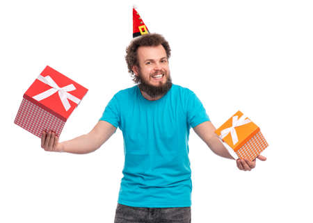 Crazy bearded Man with funny Curly Hair in little Christmas hat holding gift boxes. Happy guy in Santa hat, isolated on white background. Holidays concept.の写真素材