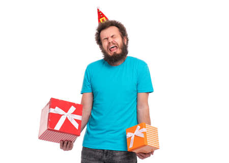 Offended Crazy bearded Man with funny Curly Hair in little Christmas hat holding gift boxes and crying. Sad screaming guy in Santa hat, isolated on white background. Holidays concept.の写真素材