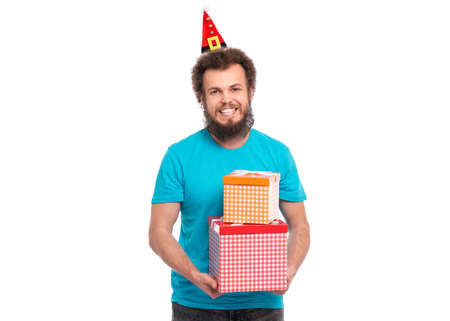 Crazy bearded Man with funny Curly Hair in little Christmas hat holding gift boxes. Happy guy in Santa hat, isolated on white background. Holidays concept.の写真素材