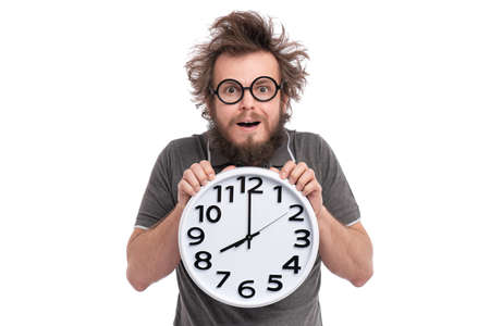 Crazy surprised bearded man with tousled hair, in glasses holding big clock, isolated on white background.の写真素材