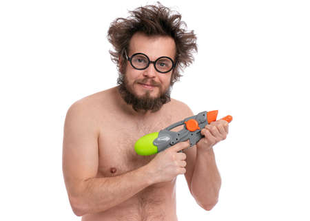 Crazy bearded Man with funny Haircut in eyeglasses, ready for fun at sunny beach. Happy and silly tourist, isolated on white background. Cheerful naked man holding Water Gun.の写真素材