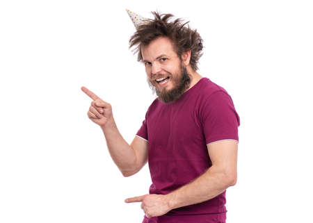 Crazy bearded Man with funny Haircut in birthday cap, isolated on white background. Happy guy smiling, looking at camera and showing something. Holidays, Emotions and Signs concept.の写真素材