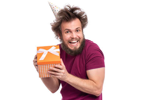 Crazy bearded Man with funny Haircut in birthday cap, isolated on white background. Happy guy holding gift box. Holidays concept.の写真素材