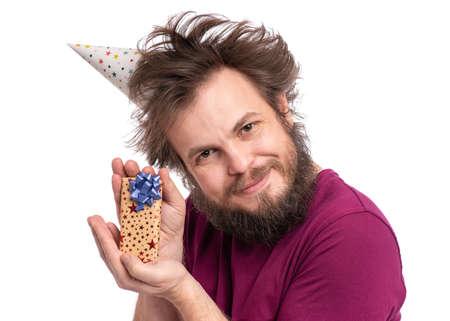 Crazy bearded Man with funny Haircut in birthday cap, isolated on white background. Happy guy holding smaill gift box. Holidays concept.の写真素材