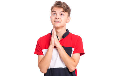 Portrait of teen boy praying, isolated on white background. Cute caucasian teenager with hands folded in prayer hoping for better. Child asking God for good luck, success or forgiveness.の写真素材