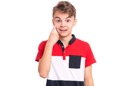 Portrait of smiling teen boy showing his eye. Child pointing with finger to eye. Caucasian young teenager, isolated on white background. Eyesight control. Medicine, people and health concept.の写真素材