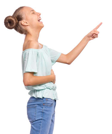 Excited teen girl pointing fingers away at copyspace - side view, isolated on white background. Cute teenager smiling and laughing pointing fingers at something. Happy child looking away - profile.の写真素材