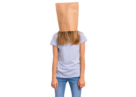 Portrait of teen girl with paper bag over her head, isolated on white background. Shy child pulling paper bag over her head. Teenager cover head with bag posing in studio.