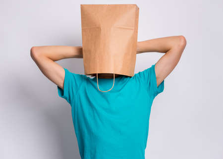 Portrait of teen boy, with paper bag over head taking rest, on gray background. Time to relax. Child holding hands behind his head having time-out.の写真素材