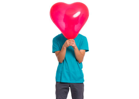 Teen boy hiding behind red heart shaped balloon. Child holding symbol of love, family, hope. Celebration of Saint Valentines Day. Teenager cover face isolated on white background.の写真素材