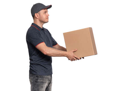 Portrait of Delivery man in cap holding big cardboard box. Handsome man looking on camera. Courier - profile view, isolated on white background.の写真素材