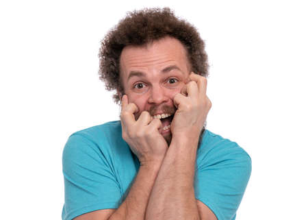 Portrait of screaming bearded man with funny Haircut bites his nails and looks worried. Scared crazy man, isolated on white background. Guy afraid and shocked. Emotions and signs concept.の写真素材