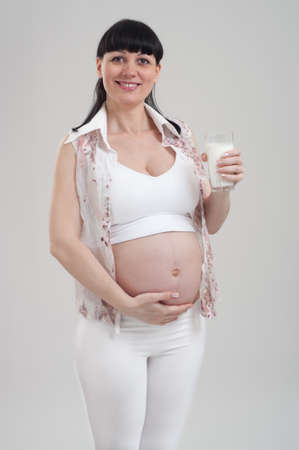 Beautiful pregnant woman holding glass of milk on gray background. Healthy nutrition and pregnancy. Happy pregnant young woman drinking milk for baby health.の写真素材