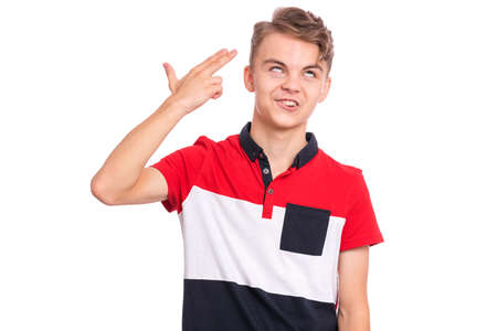 Portrait of displeased teen boy doing gun gesture. Caucasian young teenager point fingers to head as if he about shoot himself. Child holding symbolic gun isolated on white background.の写真素材