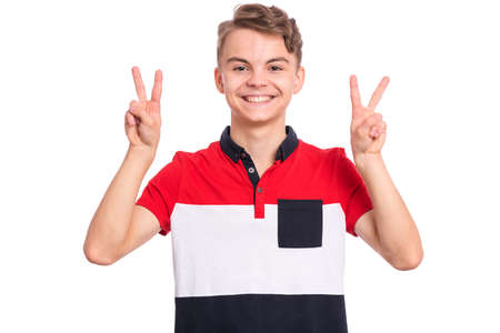 Portrait of teen boy making Victory gesture, isolated on white background. Handsome young teenager smiling and showing victory sign. Happy cute caucasian child doing victory symbol.の写真素材