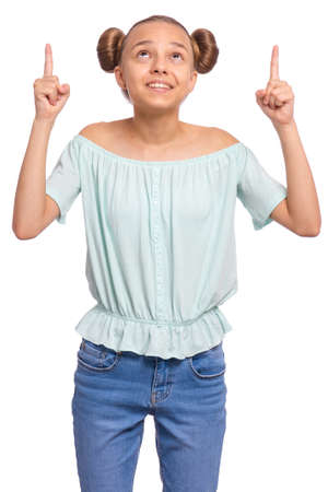 Portrait of teen girl pointing fingers up at copyspace, isolated on white background. Beautiful caucasian young teenager attracted by attention at something. Happy child looking up.の写真素材