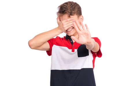 Portrait of teen boy doing stop sign with palm of hand and covering eyes with hand. Human facial emotion. Caucasian teenager isolated on white background. Child making stop gesture.の写真素材