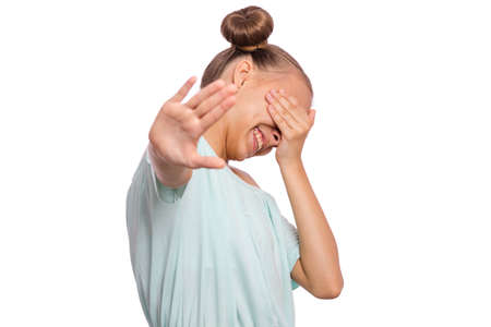 Portrait of teen girl doing stop sign with palm of hand and covering eyes with hand. Human facial emotion. Beautiful caucasian teenager isolated on white background. Child making stop gesture.の写真素材