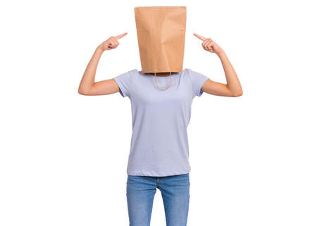 Portrait of teen girl show fingers paper bag over head, isolated on white background. Child pointing fingers at head with bag posing in studio. Teenager pulling paper shopping bag over head.の写真素材