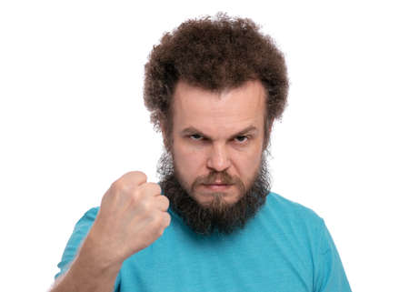 Portrait of adult bearded man showing fist with angry expression, isolated on white background. Crazy male showing fist. Upset and mad caucasian man with funny curly hair in rage looking furious.の写真素材