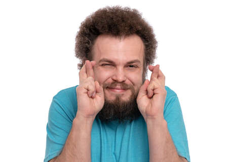 Portrait of bearded man with funny curly hair crossing his fingers and wishing for good luck. Happy crazy male smiling, isolated on white background.の写真素材