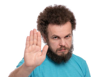 Portrait of bearded man with funny curly hair doing stop sign with palm of hand, isolated on white background. Angry male making stop gesture with negative and serious facial expression.の写真素材