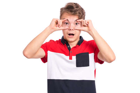 Emotional portrait of teen boy - he holds his eyes with his fingers. Funny caucasian young teenager keeping his eyes and mouth opened. Surprised child isolated on white background.の写真素材
