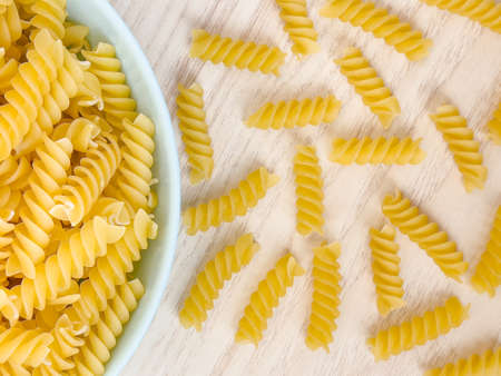 Raw dry Italian pasta in shape of spiral in bowl on wooden table at kitchen. Food background. Top view. Uncooked macaroni.の写真素材