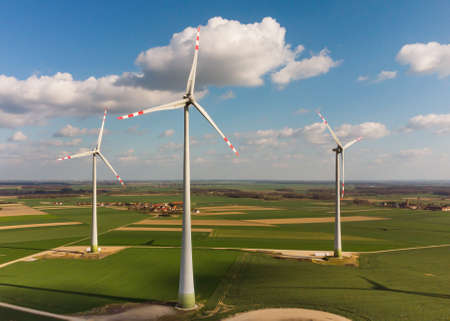 Aerial view of large wind turbines with blades in field against blue sky and white clouds. Alternative energy. Wind farm generating green energy.の写真素材