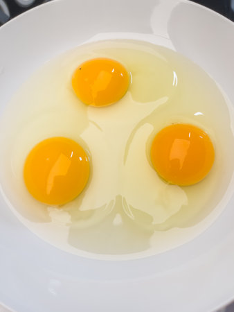 Three bright yellow raw chicken eggs in a white bowl.の写真素材