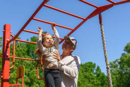 Father helps his child's daughter to climb the rope. Concept of helping young peopleの写真素材