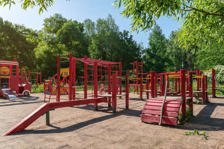 Children playground on yard activities in public park surrounded by green trees at sunlight morning. Children run, slide, swing,seesaw on modern playground. Urban neighborhood childhood concept.の写真素材