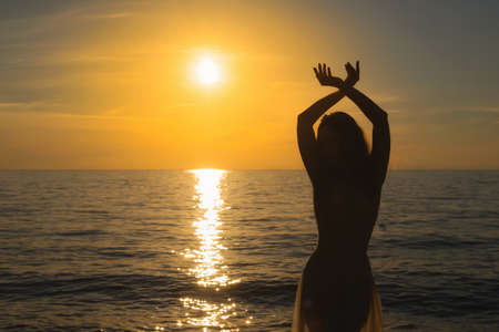 Front view of a back light of faithful woman silhouette holding sun on the beach at sunrise with a warm backgroundの写真素材