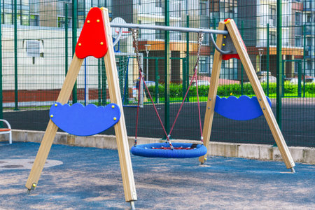 Children playground on yard activities in public park surrounded by green trees at sunlight morning. Children run, slide, swing,seesaw on modern playground. Urban neighborhood childhood concept.のeditorial素材