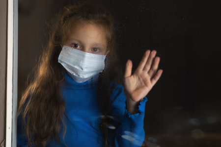 Baby girl in medical mask behind wet glass.の写真素材