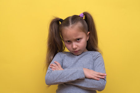A cute girl in a gray T-shirt shows emotions on a yellow background.の写真素材