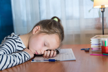 Back to school. Tired little child girl sleeping on the desk while doing homework. Education...
